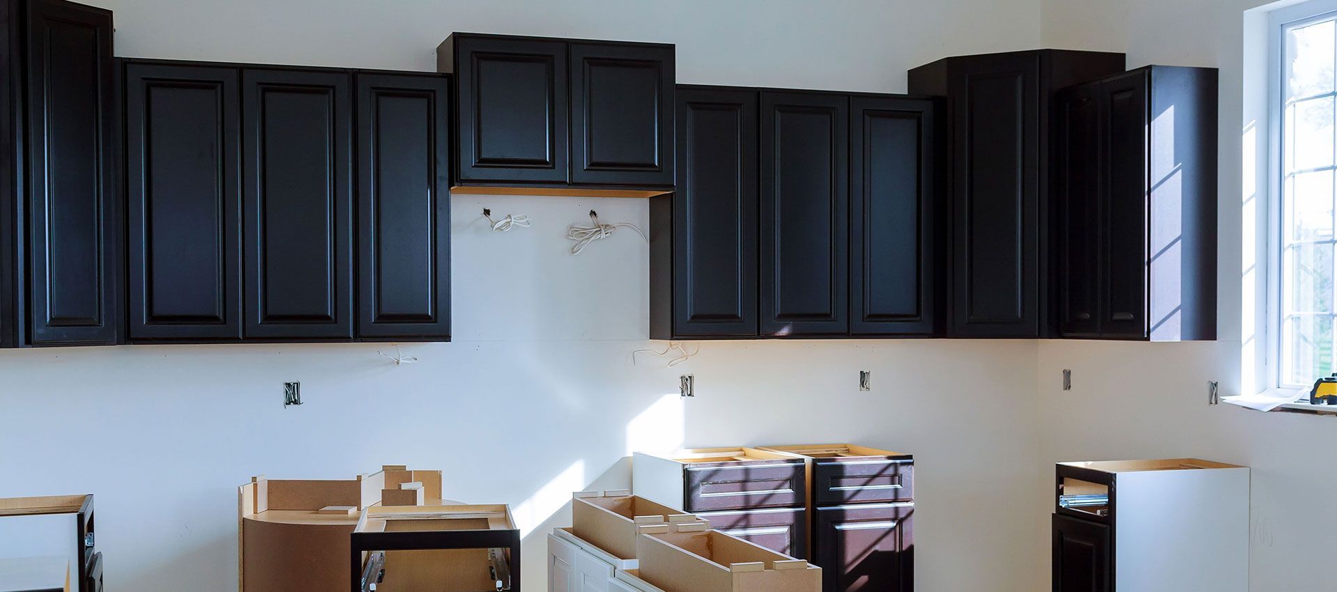 Kitchen under renovation with dark cabinets, white walls, and boxes on the floor