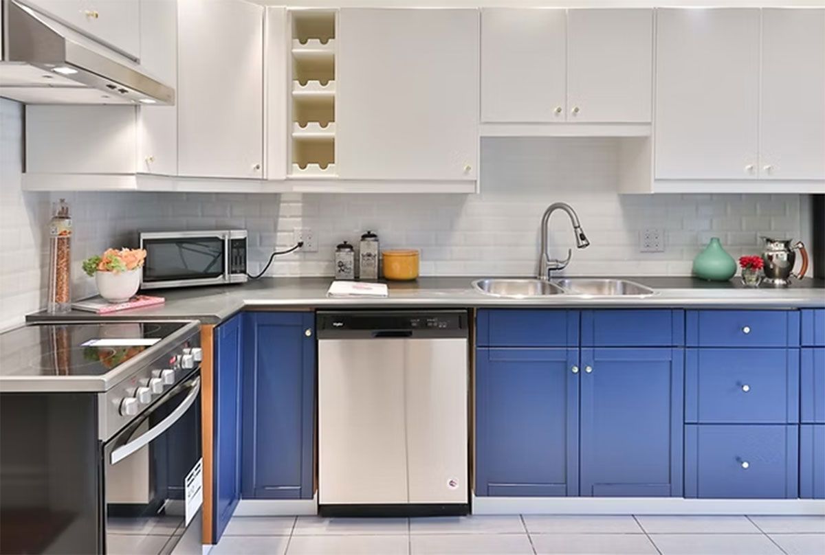 Modern kitchen with blue lower cabinets, white upper cabinets, stainless appliances, and a sink by the window