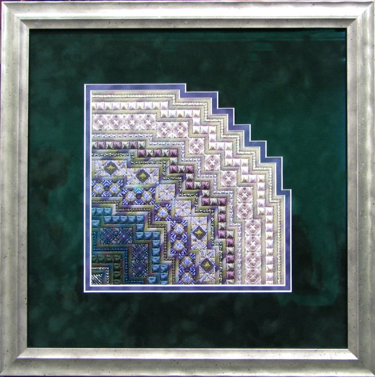 A cross stitch pattern in a silver frame on a green background