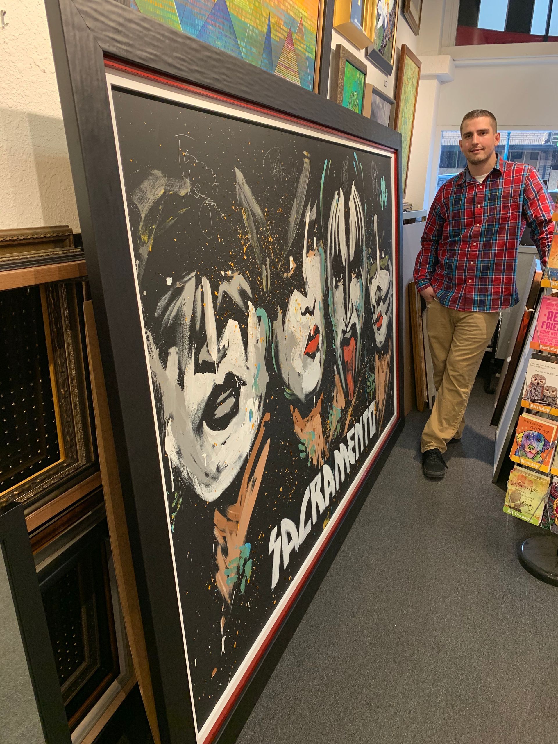 A man is standing next to a large framed kiss painting
