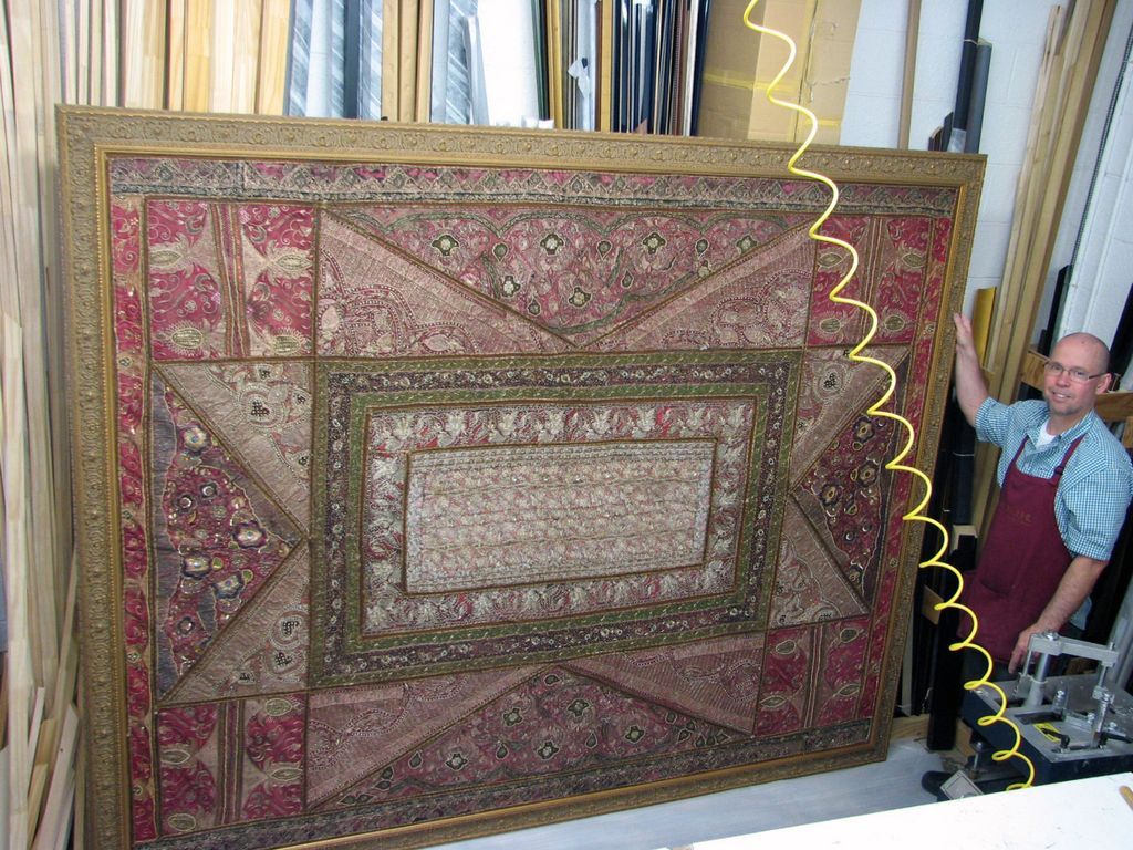 A man in an apron is standing next to a large picture frame