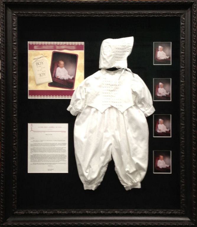 A framed picture of a baby in a white outfit