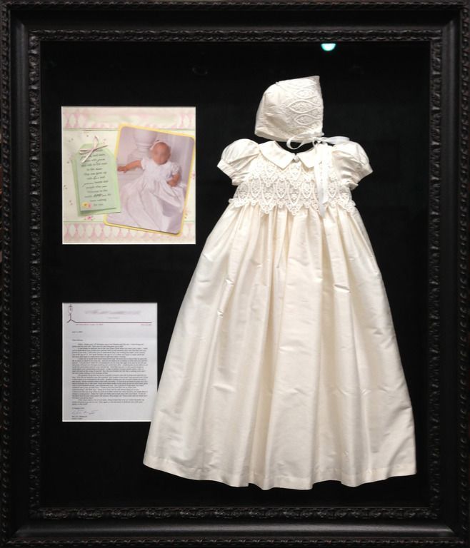 A white christening gown is in a black frame