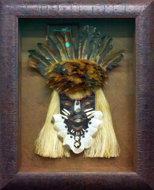 A picture of a native American mask in a brown frame