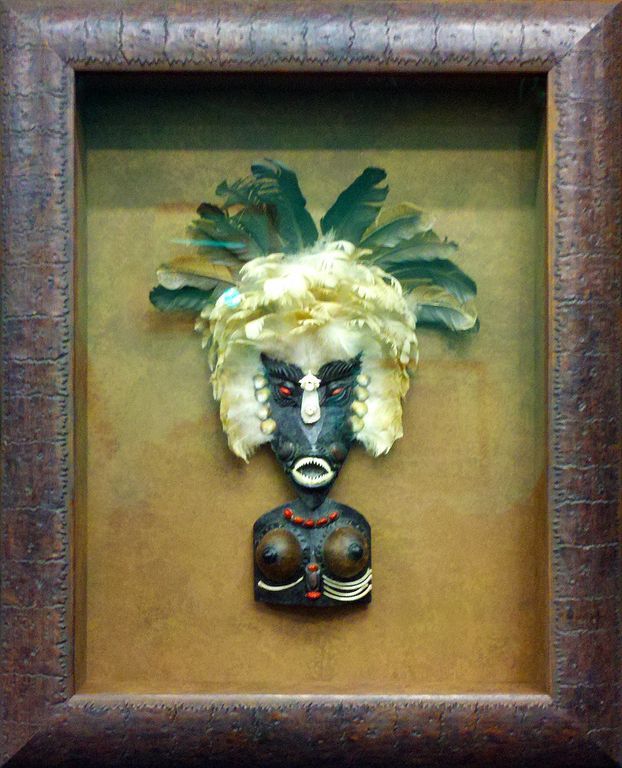 A framed picture of a mask with feathers on it