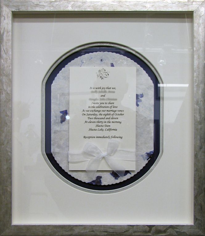 A wedding invitation is framed in a silver frame