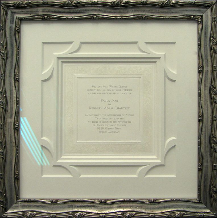 A wedding invitation is framed in a silver frame