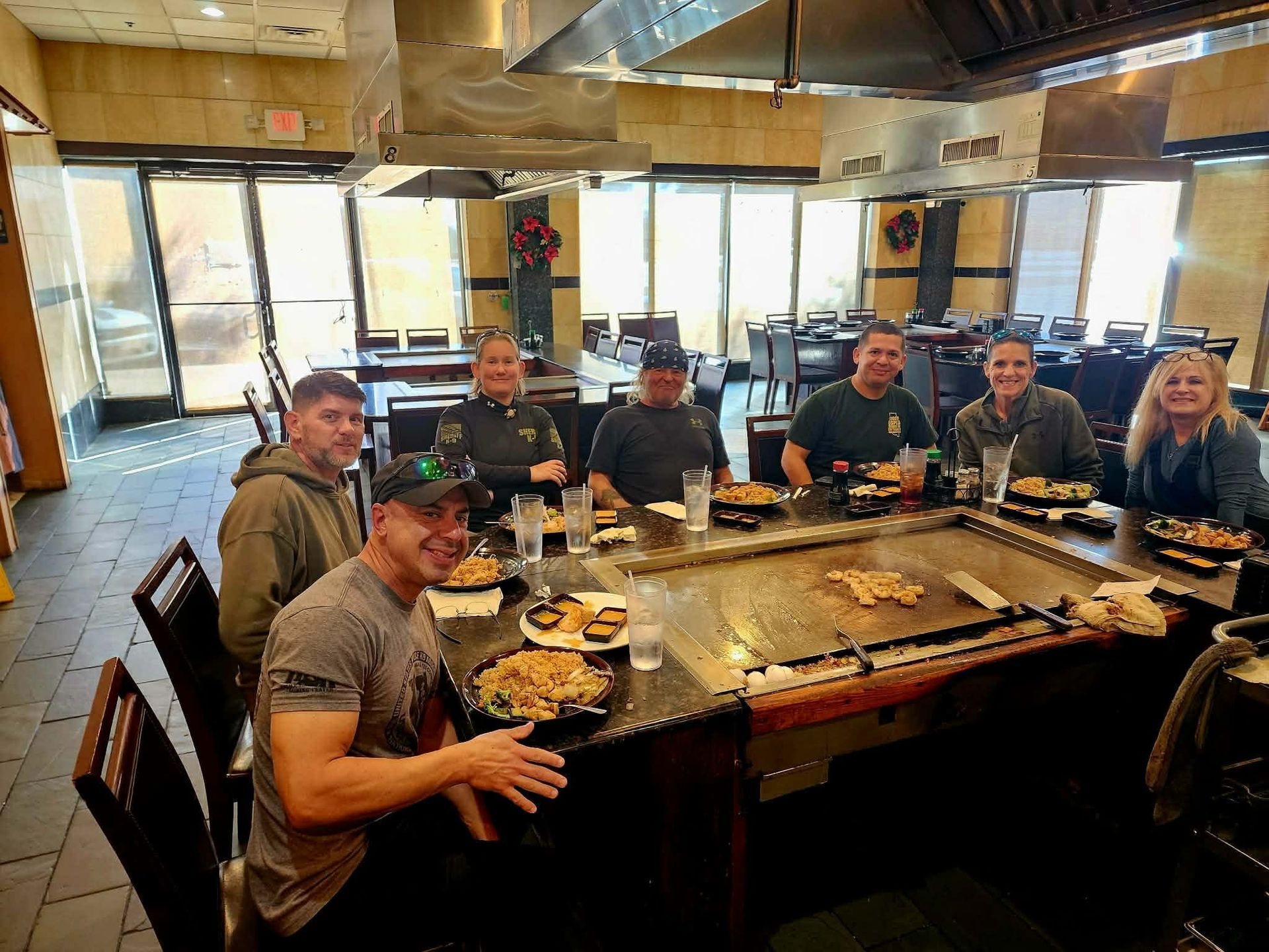 Group of people at a hibachi grill restaurant, smiling. Food and drinks on the table.