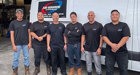 Six people in black shirts pose in front of a white van with