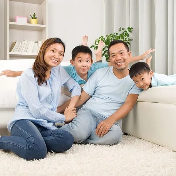 Family of four smiling, posing indoors near a sofa. Two boys playfully raise their arms.
