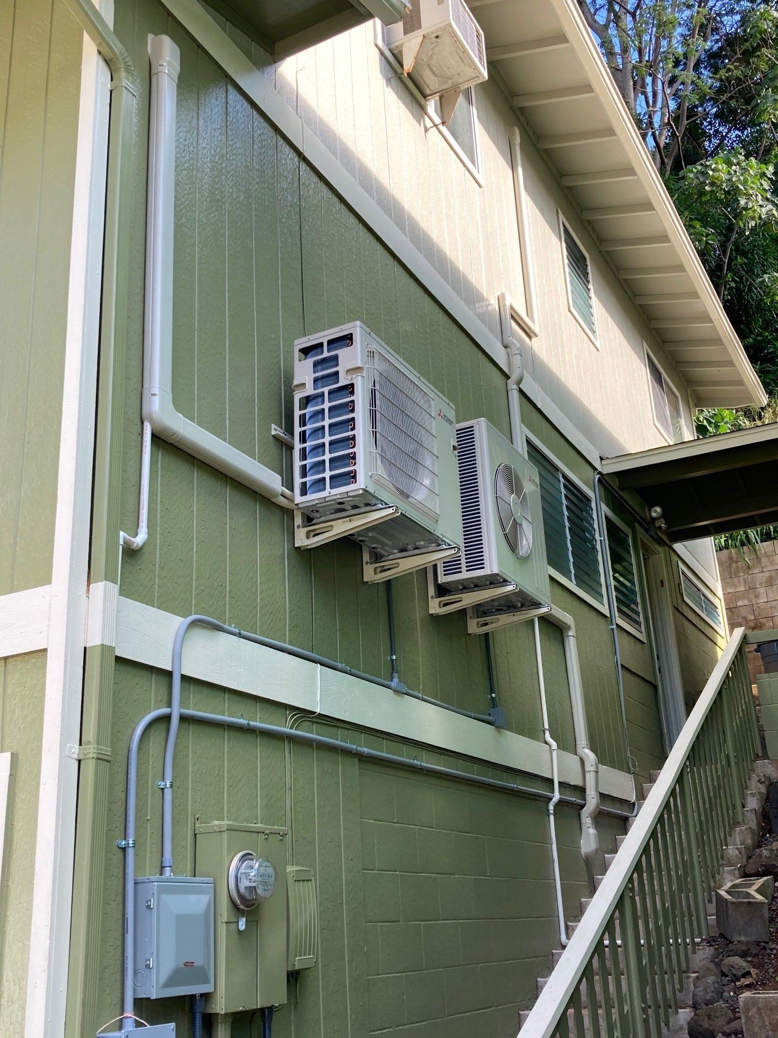 Green building exterior with air conditioning units and electrical conduit.