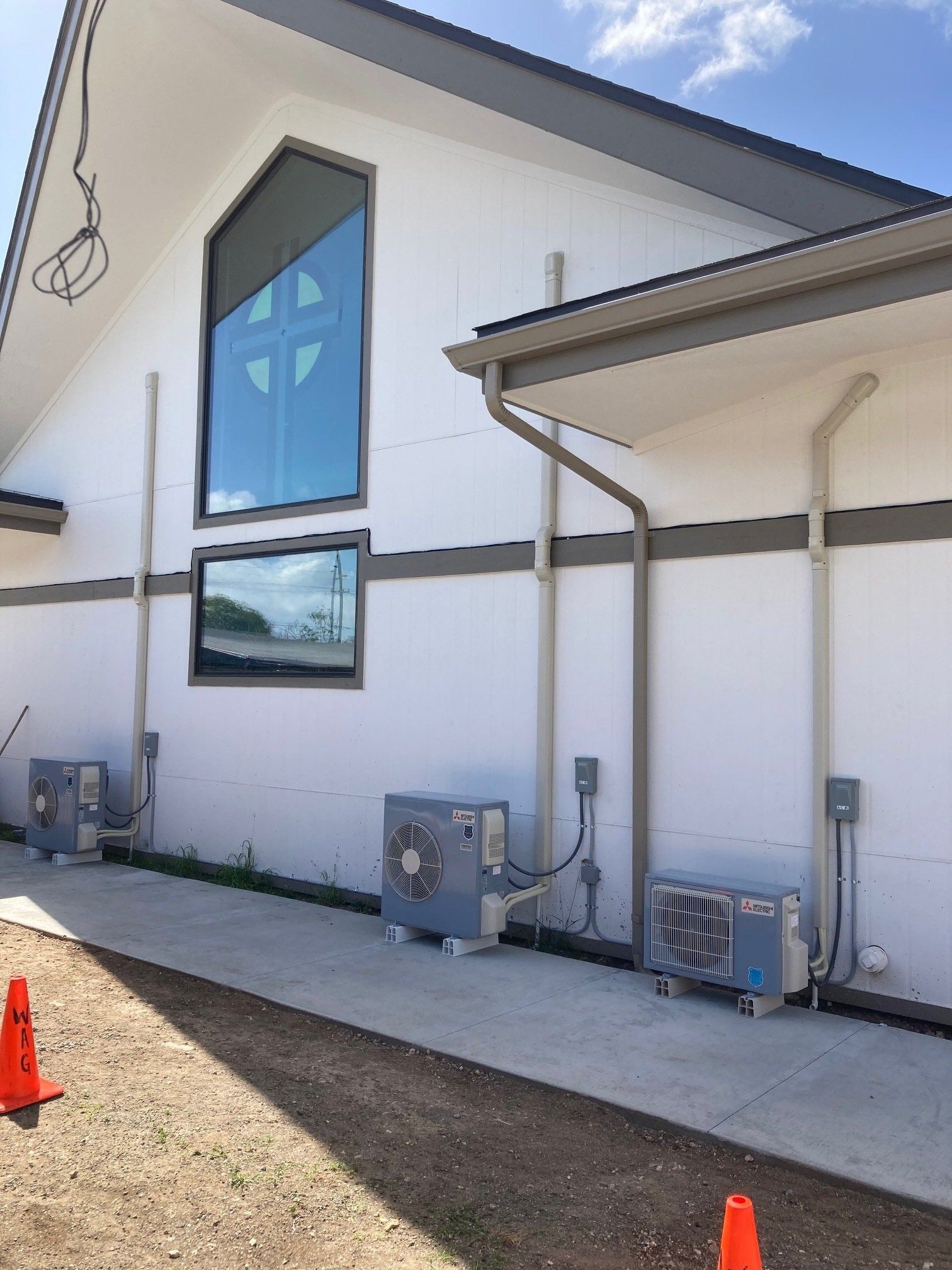 Exterior view of a white building with several AC units along the base, next to a concrete path.
