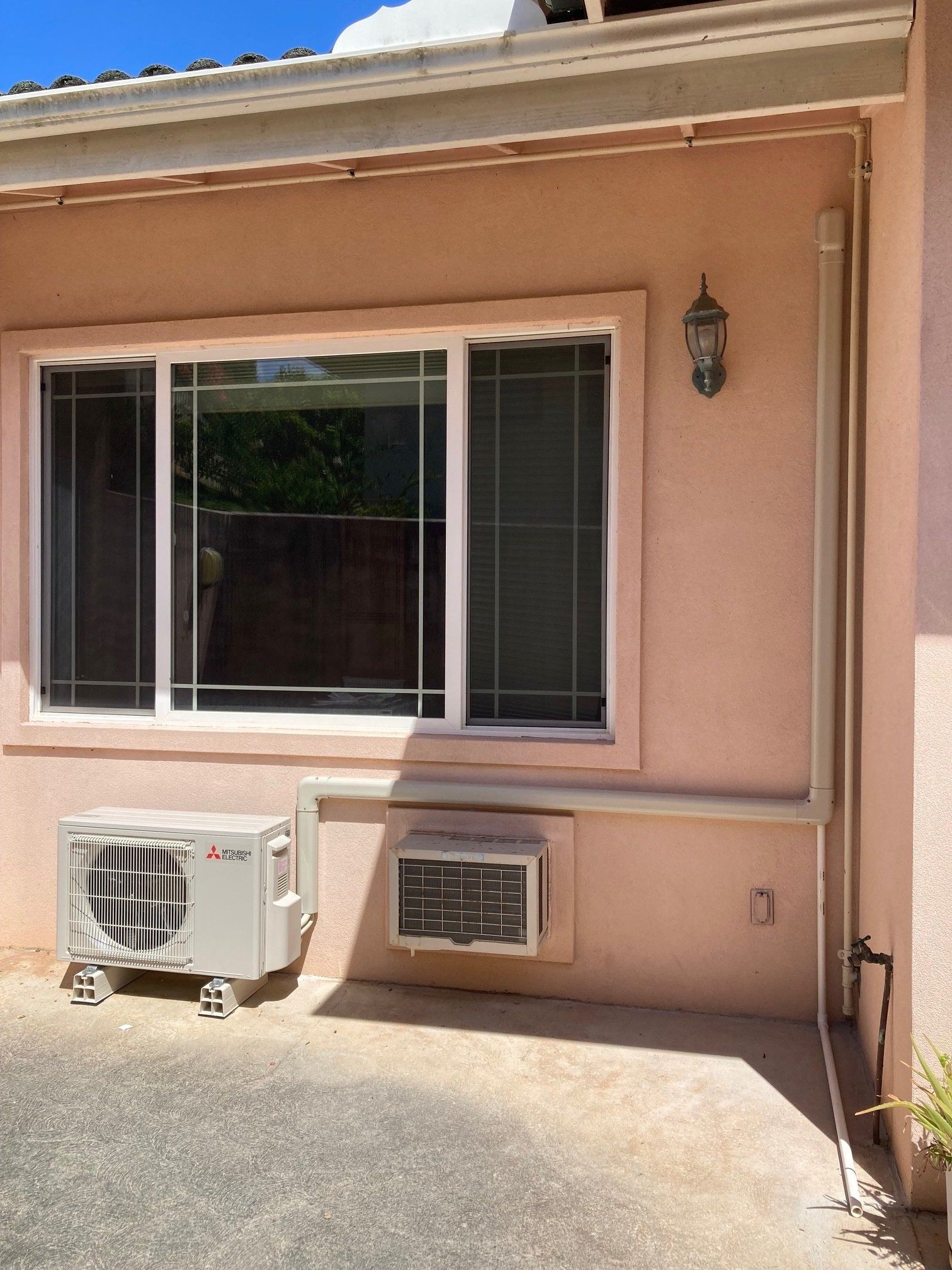 Exterior view: Window above two AC units on a peach-colored stucco wall.