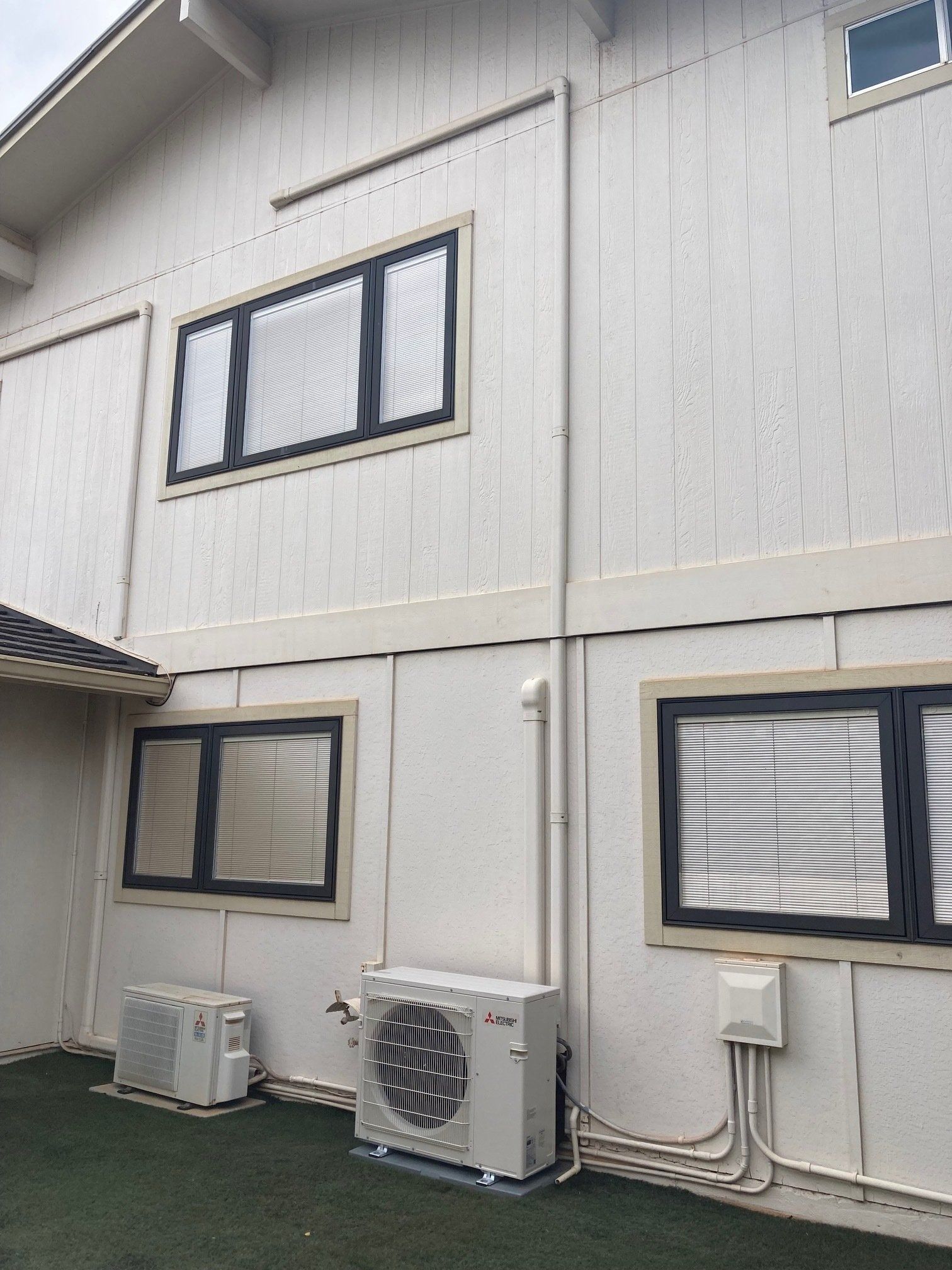 Exterior wall with three windows, two air conditioning units, and conduit.