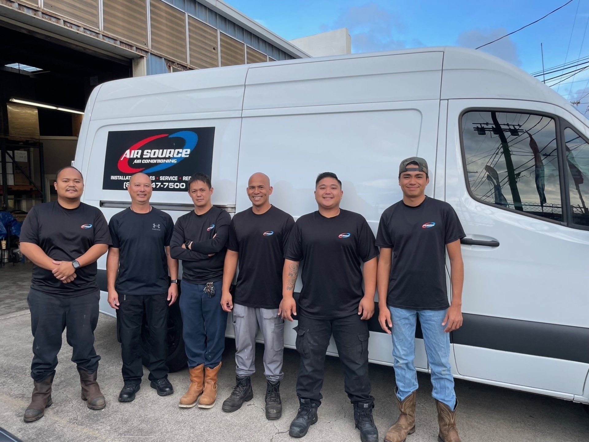 Six people in black shirts stand in front of a white van with a company logo.