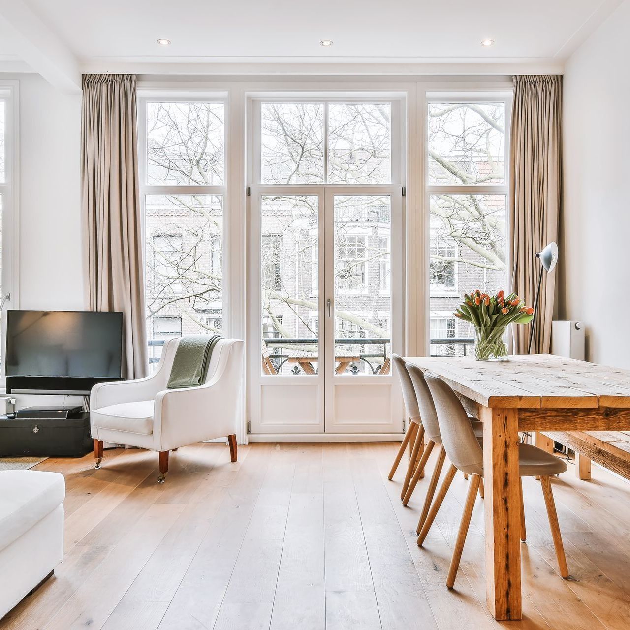 Living room with large windows, armchair, dining table, and wood floors.