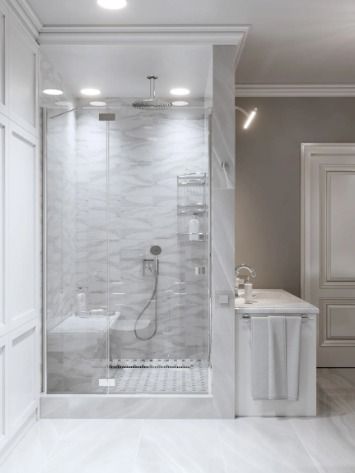 Elegant white bathroom with a glass-enclosed shower, marble-like tiles, and built-in seating.