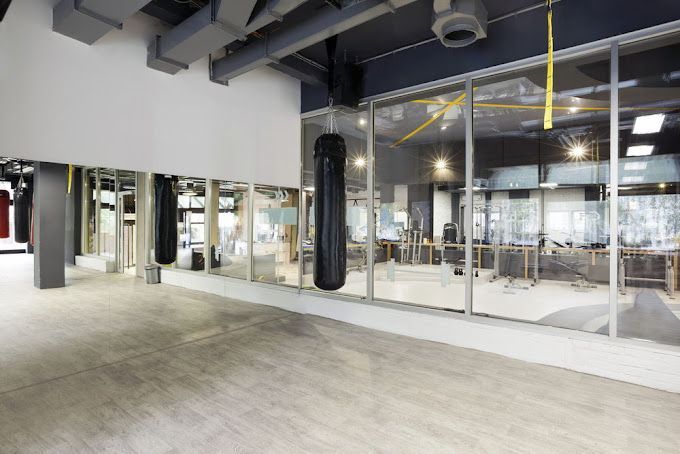 Empty boxing gym with punching bag, mirrors, and large windows.