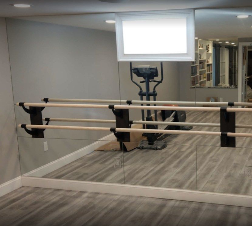 Dance studio with a barre, mirror wall, and elliptical machine; gray floor.