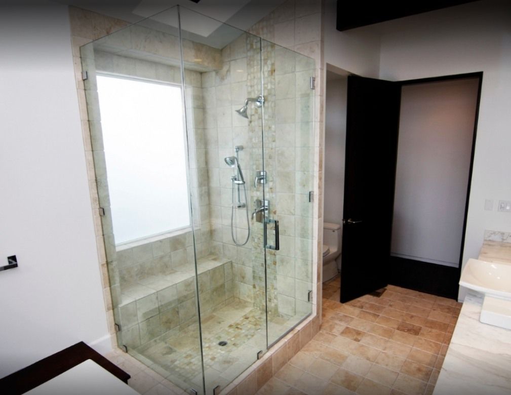 Shower with glass doors and stone tile walls, next to a partially open black door.