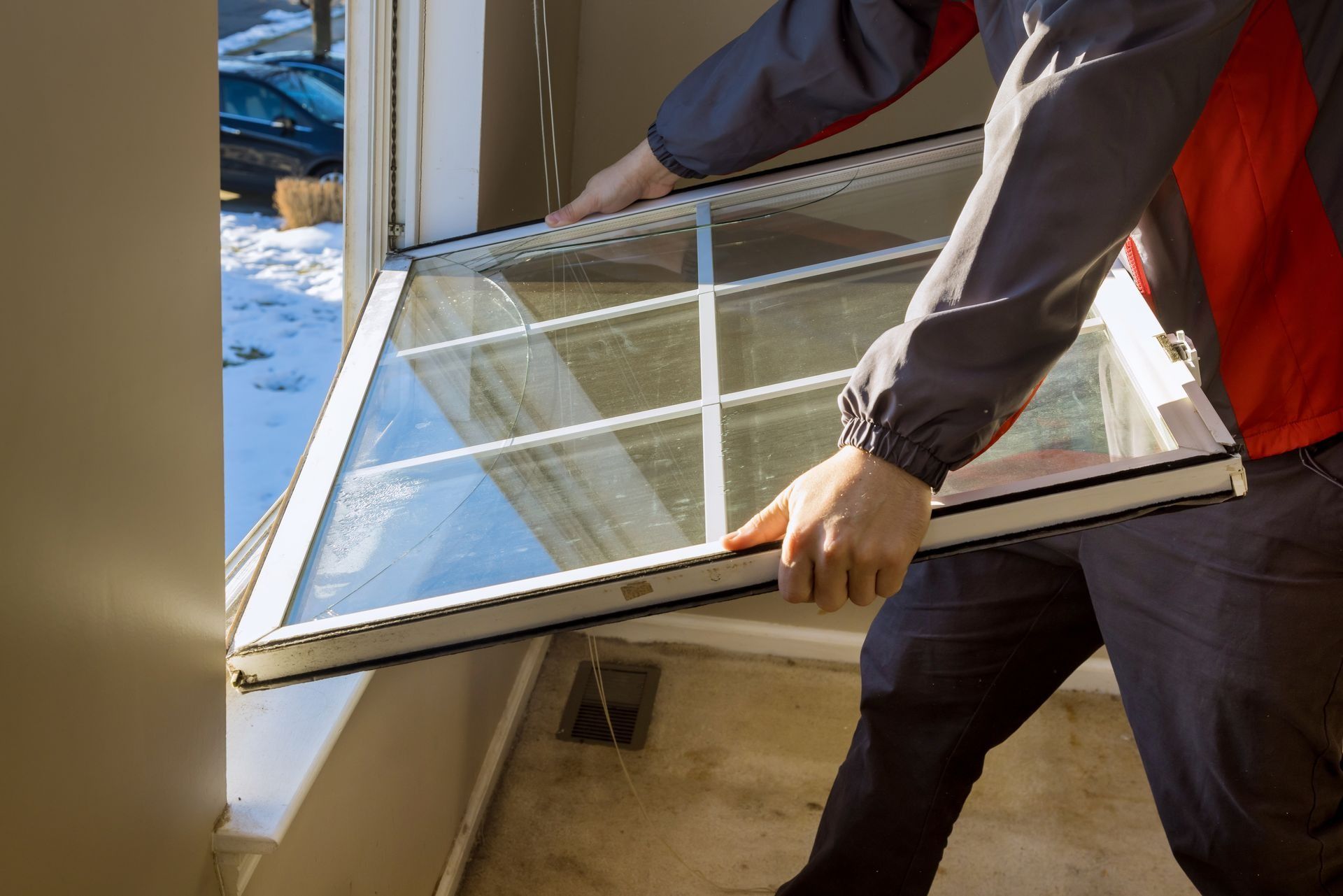 Person installing a window pane; indoor setting with snow visible outside.