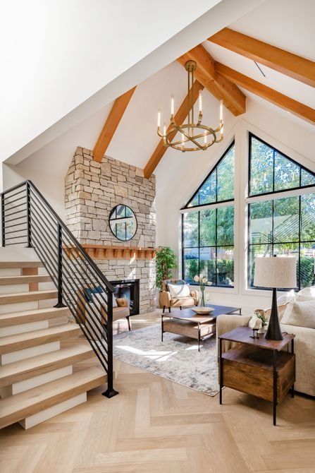 Living room with stone fireplace, staircase, vaulted ceiling, and large triangular windows.