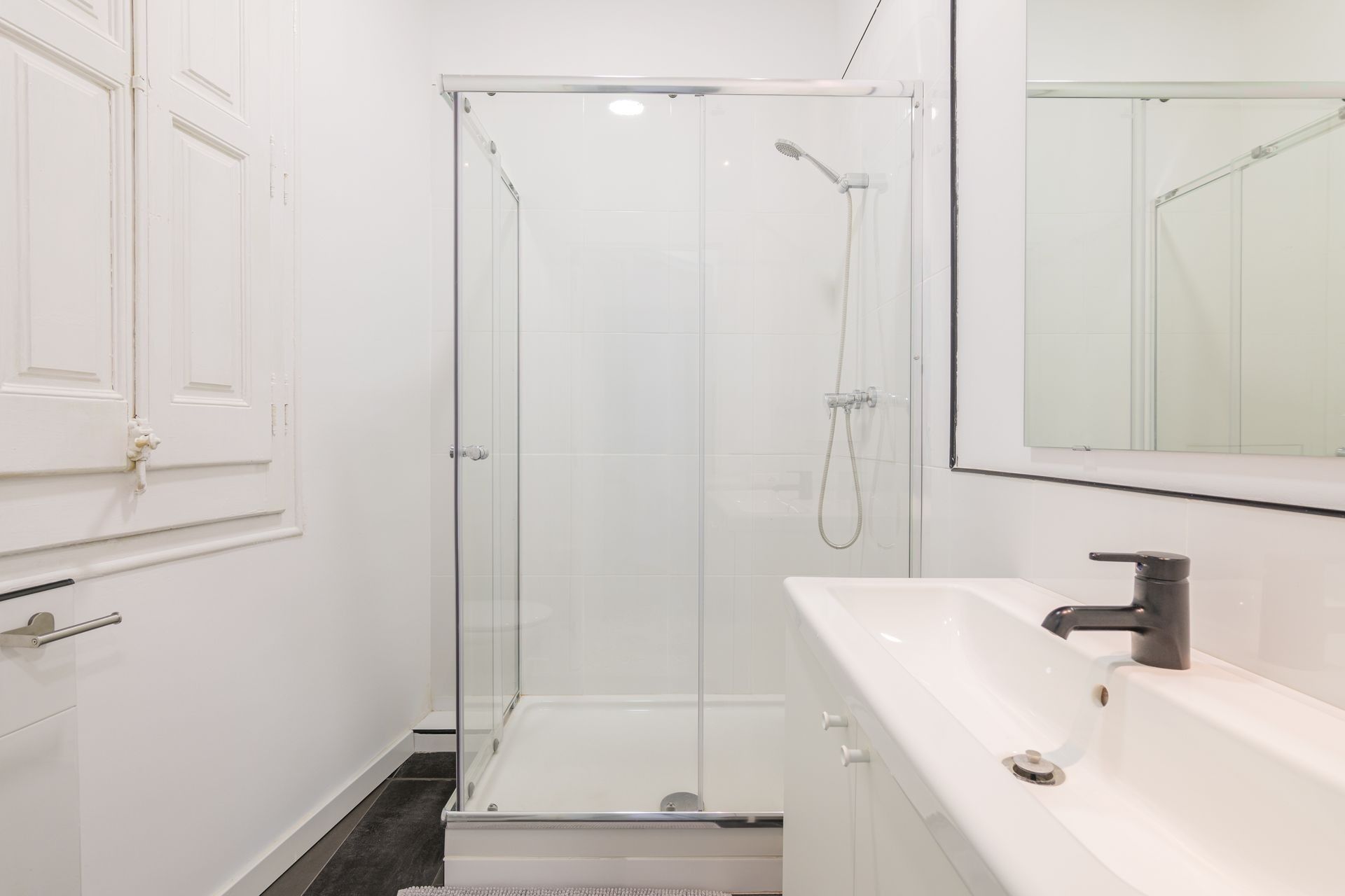 White bathroom with a glass shower, sink, and mirror.