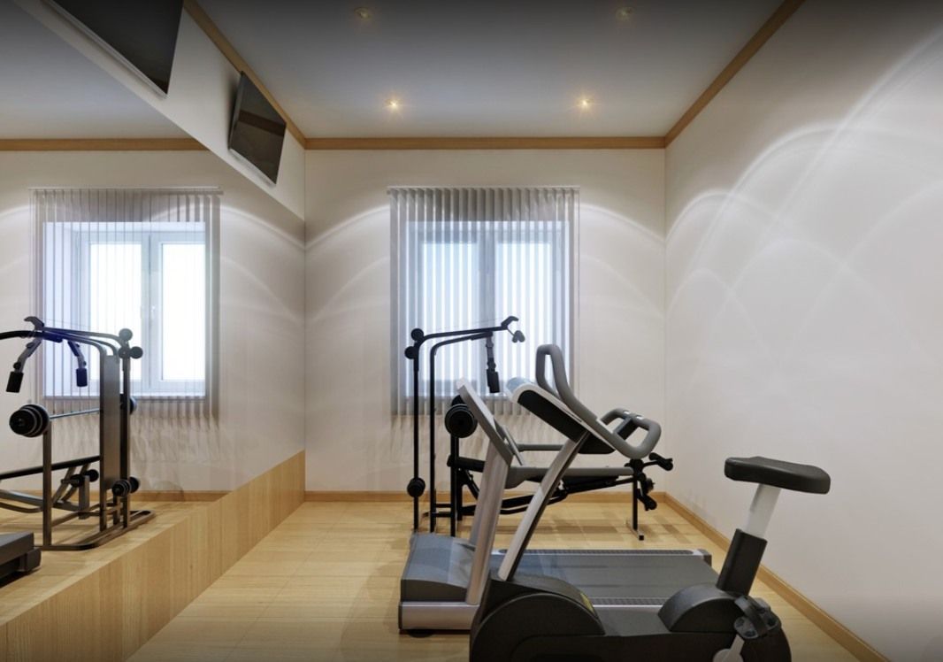 Home gym with exercise equipment: weight machine, stationary bike, treadmill; neutral walls, wood floor.