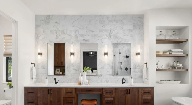 Bathroom with three mirrors over a dark wooden vanity and marble tile wall.
