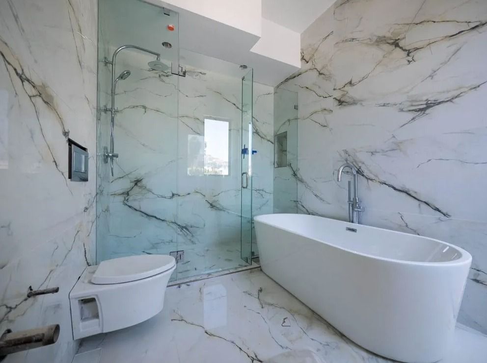 Luxurious bathroom with marble walls, glass shower, soaking tub, and wall-mounted toilet.