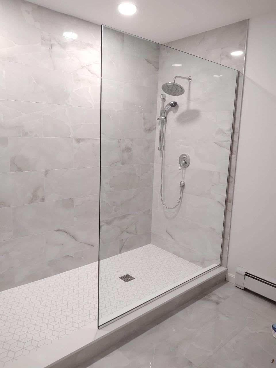 Modern shower with marble-look tile, glass enclosure, chrome fixtures, and white hex tile floor.