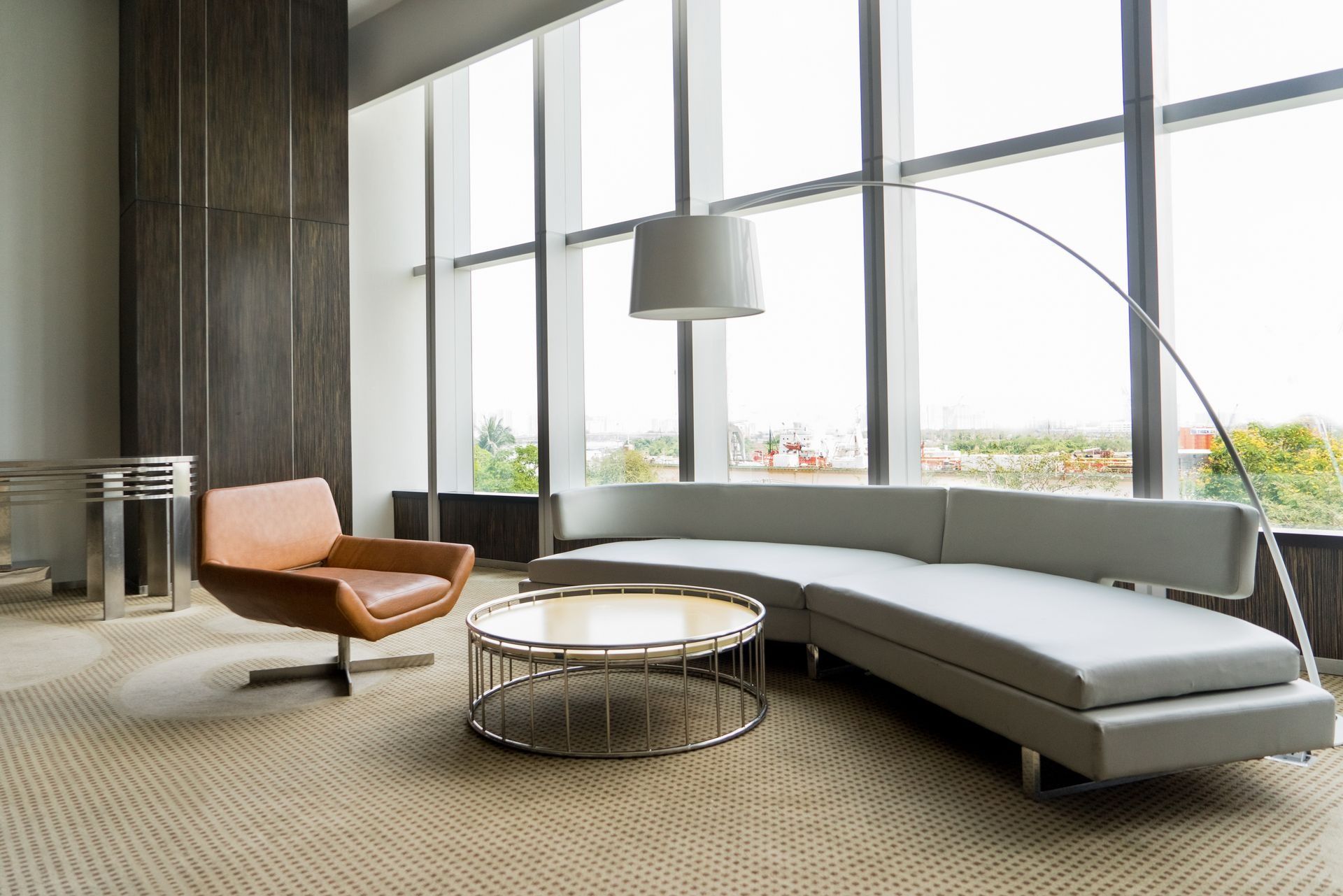 Modern living room with a curved sofa, armchair, and round coffee table in front of large windows.