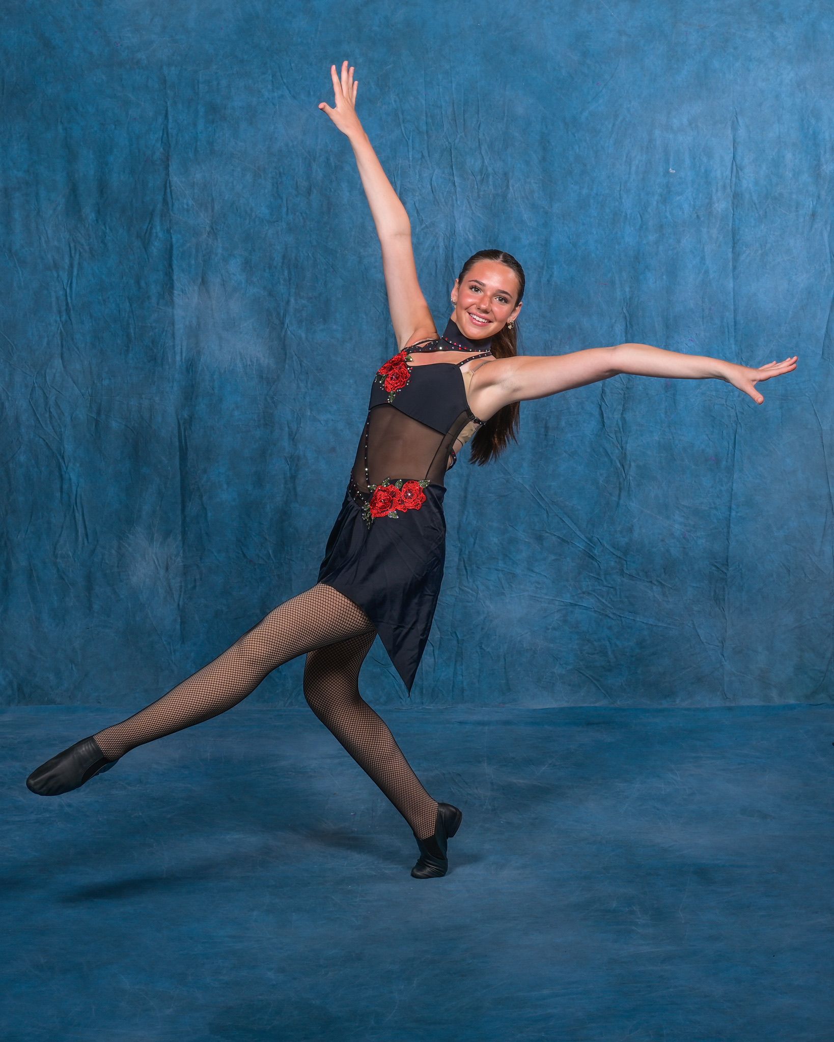 Female dancer in black and red costume with cheetah print leggings, arms outstretched against a blue backdrop.