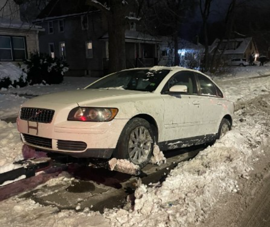 White Volvo car stuck in a snowbank on a street at night.