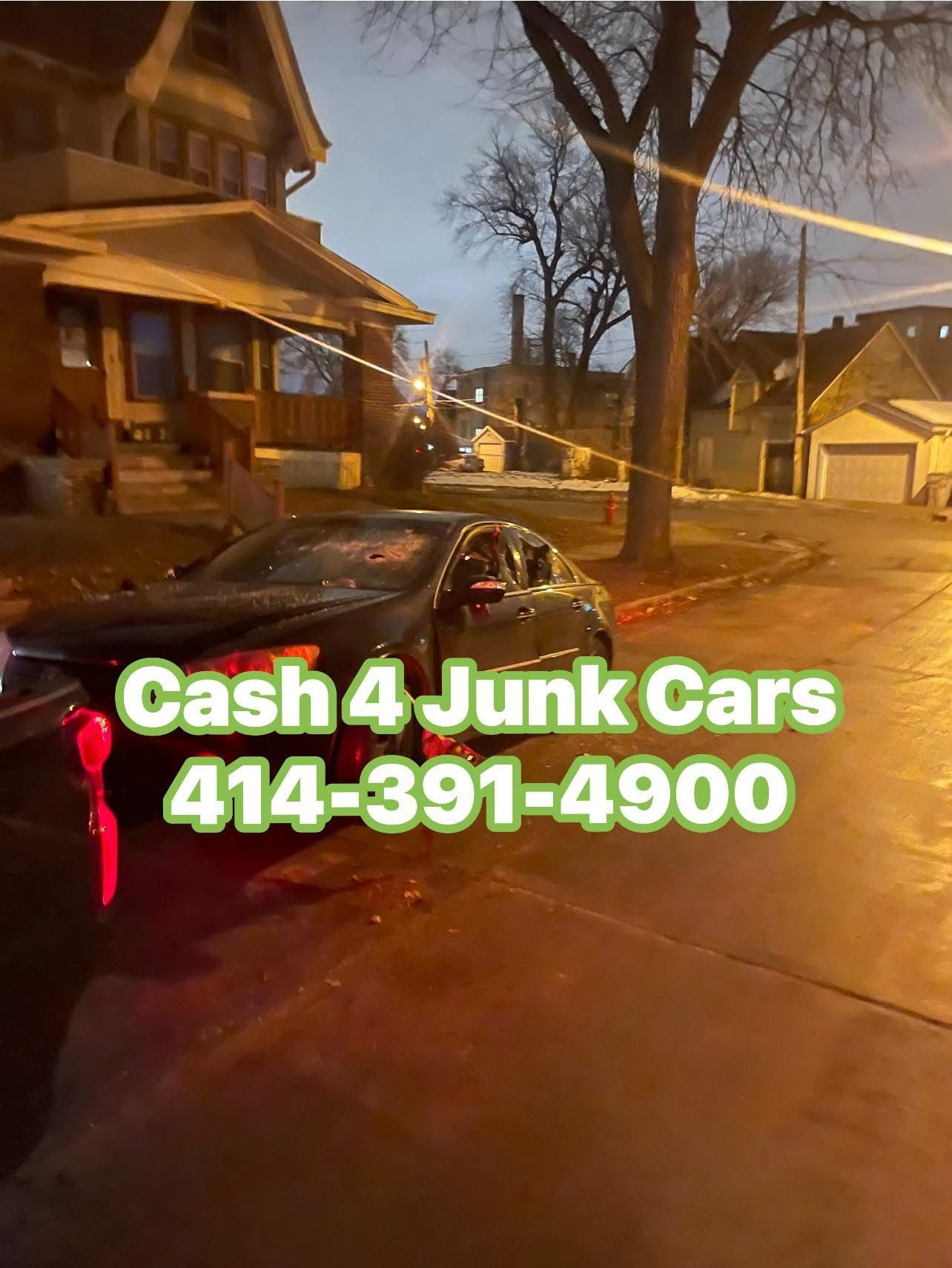 A damaged black car on a street, with a house in the background. 