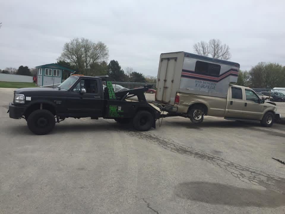 Tow truck hauling a beige moving van and pickup truck in a parking lot