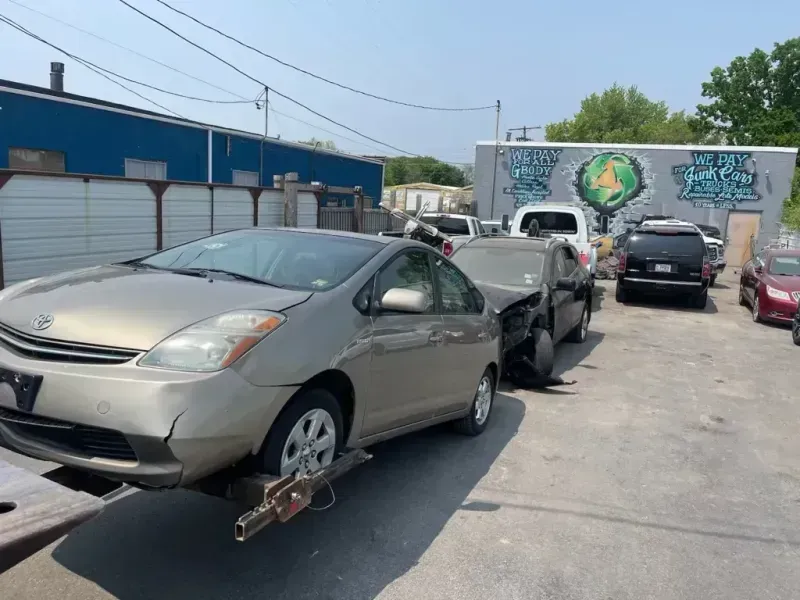 A beige Toyota Prius being towed on a sunny day in front of a building with graffiti.