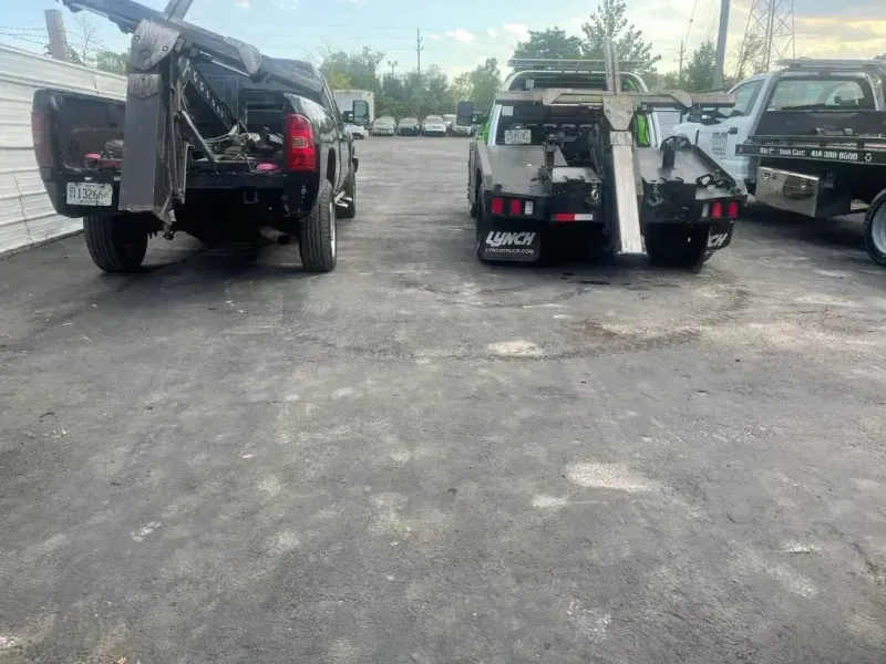 Two tow trucks parked on a paved lot; one with the bed open, both with towing equipment.