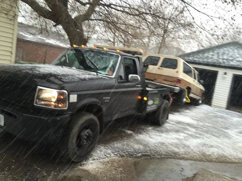 Black tow truck hauling a tan van in snowy conditions.