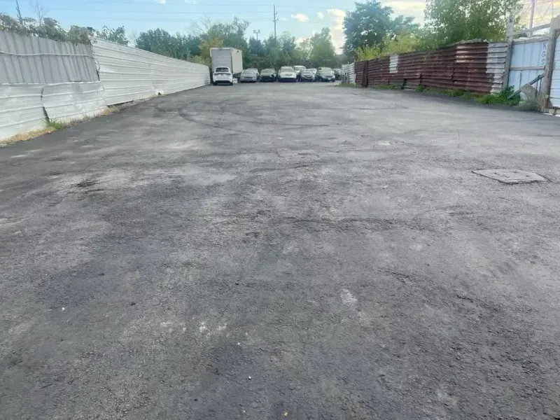 Asphalt parking lot; parked vehicles in the distance, a fence on either side.