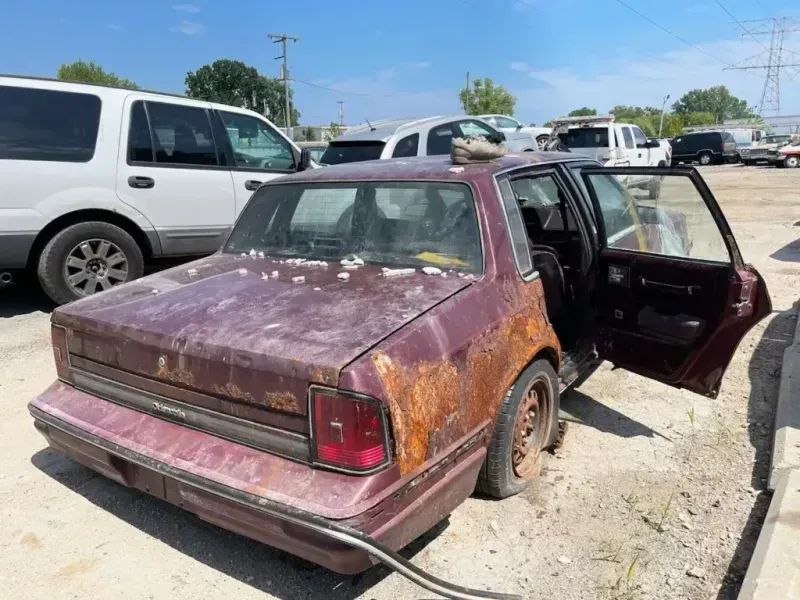 Rusty maroon car with open door, parked outside.