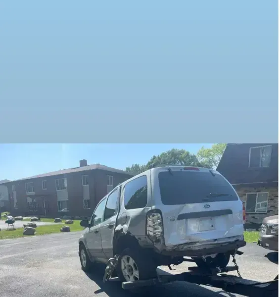 Silver SUV damaged in a collision, being towed away on a flatbed trailer in front of an apartment complex.