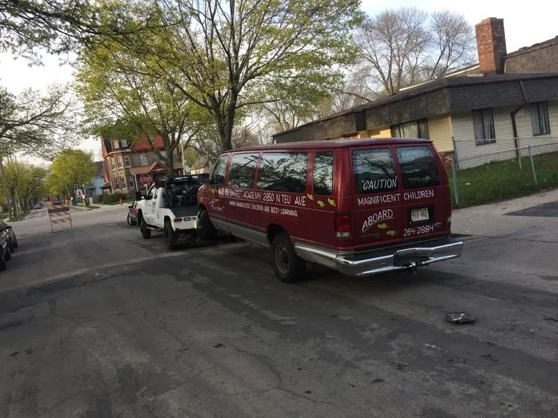 A red van being towed on a residential street. The van has text reading 