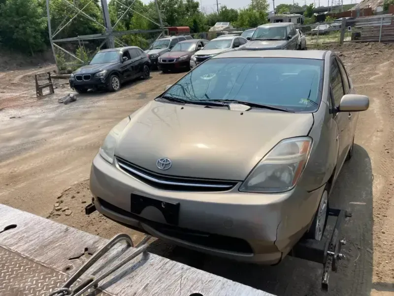 Gold Toyota Prius on a tow truck, other cars in the background in a lot on a sunny day.