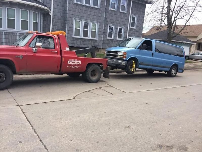 Red tow truck towing a blue van on a city street.