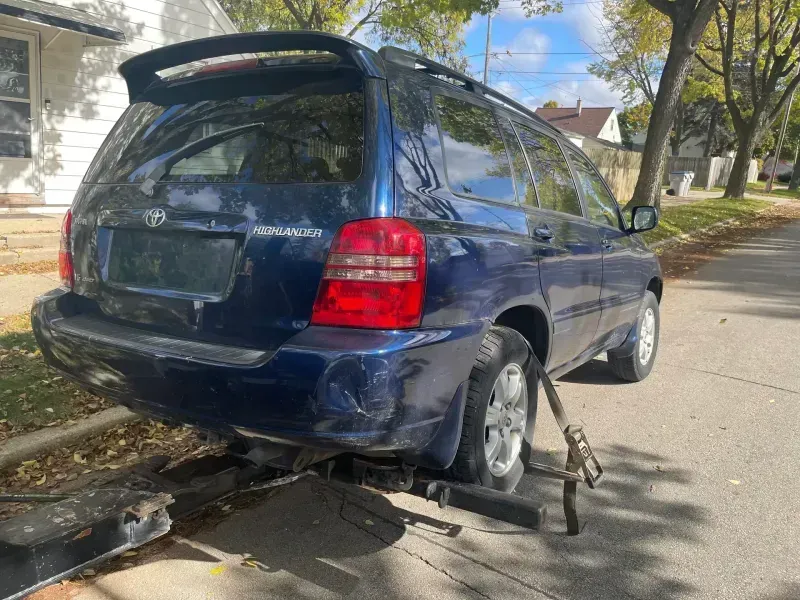 Damaged blue Toyota Highlander on a tow truck, rear end dented.