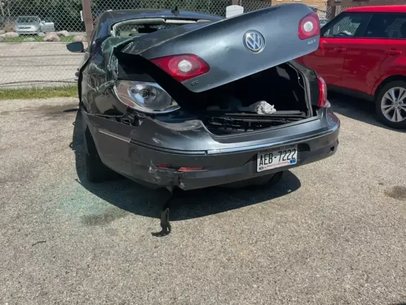 Damaged gray Volkswagen sedan with open trunk, rear end collision visible, parked on pavement.