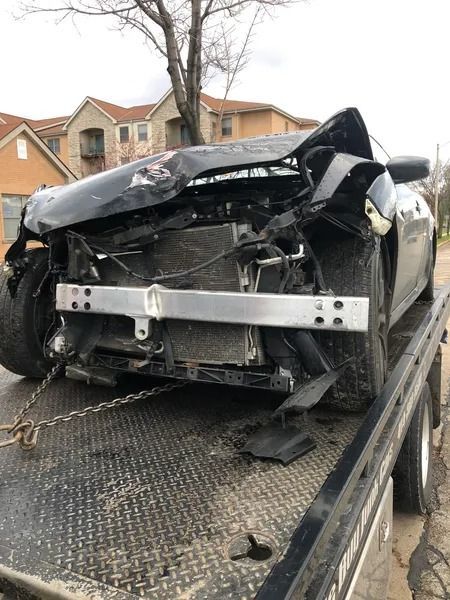 A severely damaged black car on a tow truck. The front end is completely crushed.