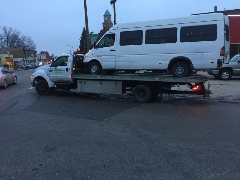 Tow truck carrying a white passenger van on a city street.