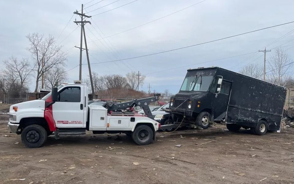 Tow truck towing a black box truck on a cloudy day. The setting appears to be a lot.